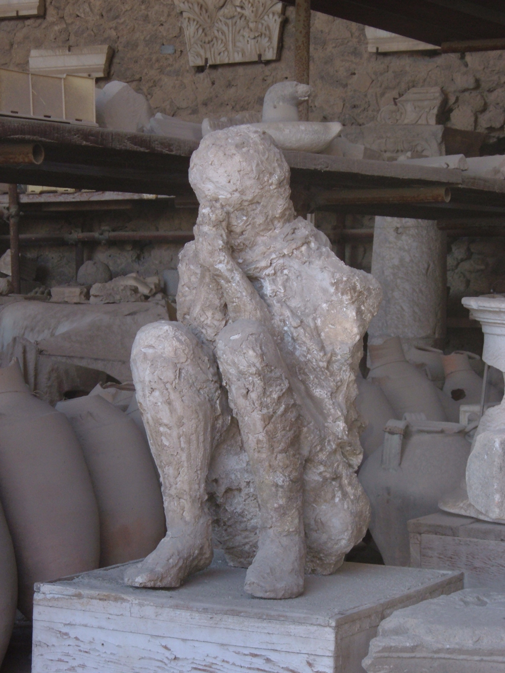 a pompeii body cast shows a rocky silhouette sat with head bowed in hands